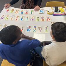 Students learning their letter recognition at table with teacher.  